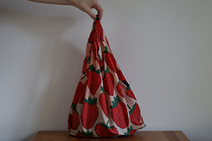 A strawberry-print bag filled with items, being held by a hand from above.